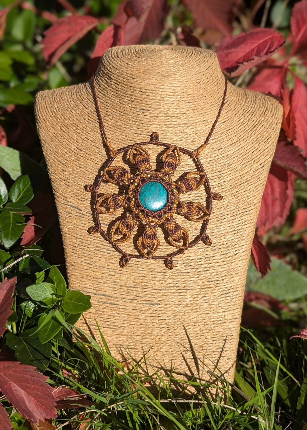 Collier micro macramé orné d'une pierre bleu au centre, posé sur un buste osier, sur fond de nature.